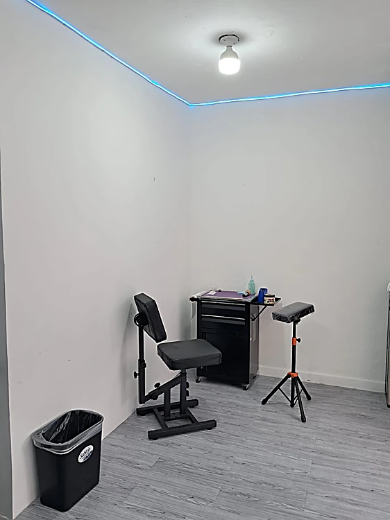 Cabina blanca con silla de tatuaje, mesa de trabajo con ruedas y una tira de luz azul en el techo