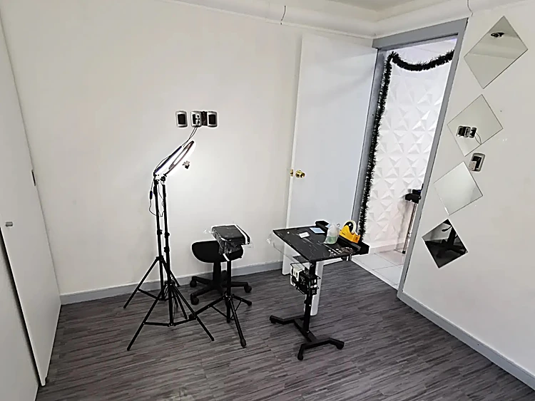 Cabina de tatuaje con aro de luz, banco y mesa de trabajo; en la pared, espejos en rombo