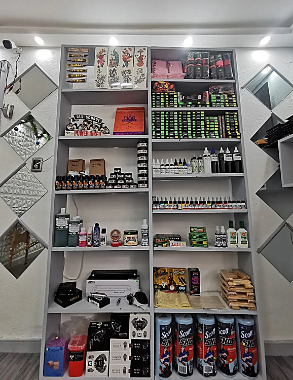 Interior del estudio: estante blanco con tintas, agujas y material de tatuaje, entre dos paredes con espejos en forma de rombo