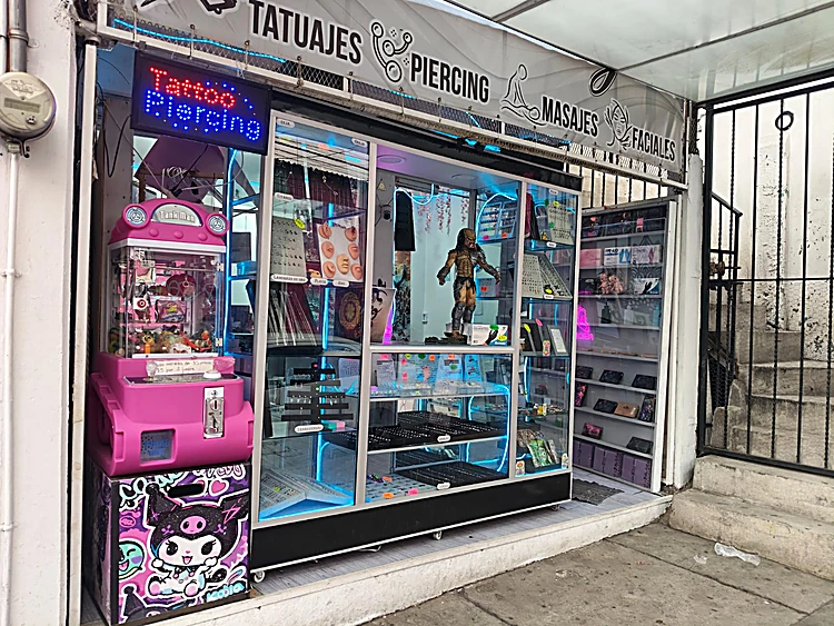 Fachada del estudio: letrero de Tatuajes, Piercing, Masajes y Faciales sobre vitrinas iluminadas con joyería de piercing