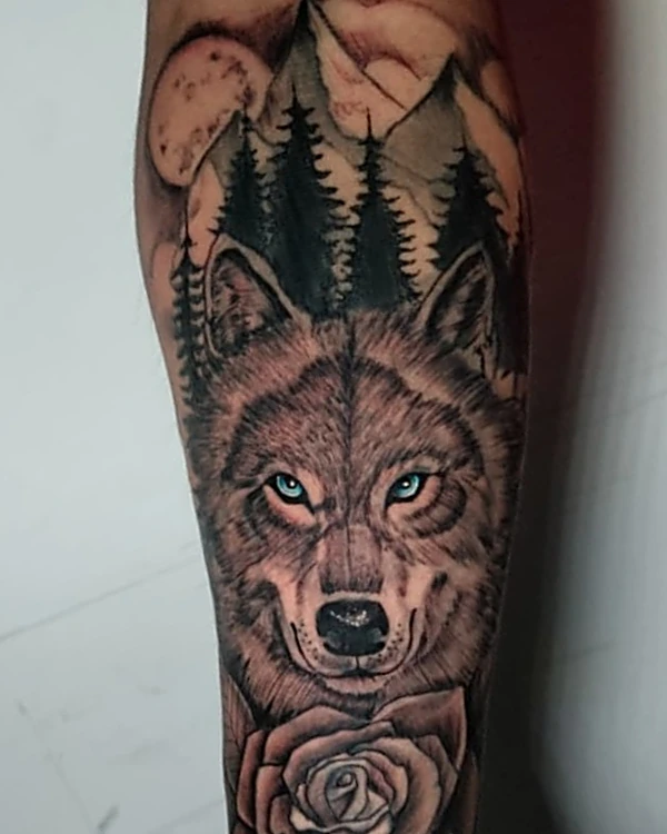 Lobo con bosque y rosa en realismo negro y gris, tatuado en el antebrazo