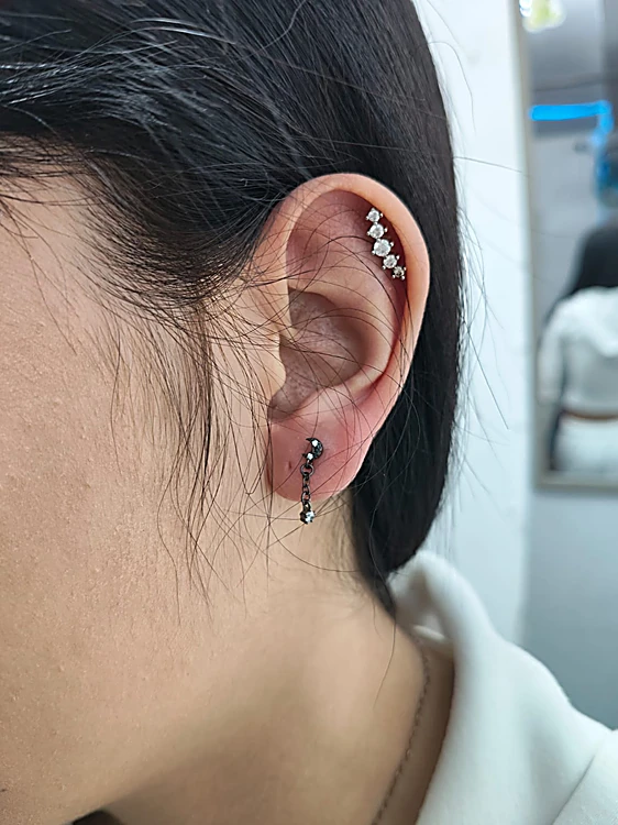 Oreja con piercing en el hélix de cuatro cristales y un arete colgante en el lóbulo